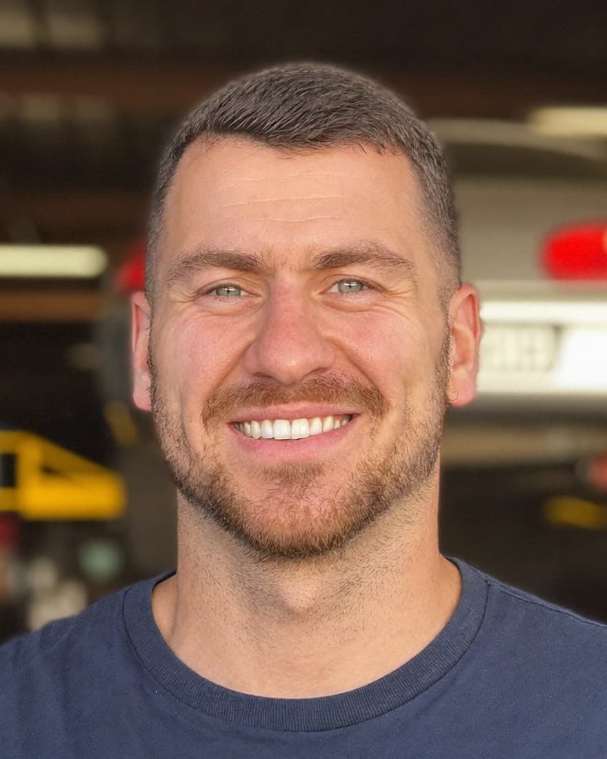 A friendly auto mechanic in a repair shop with a car on the lift